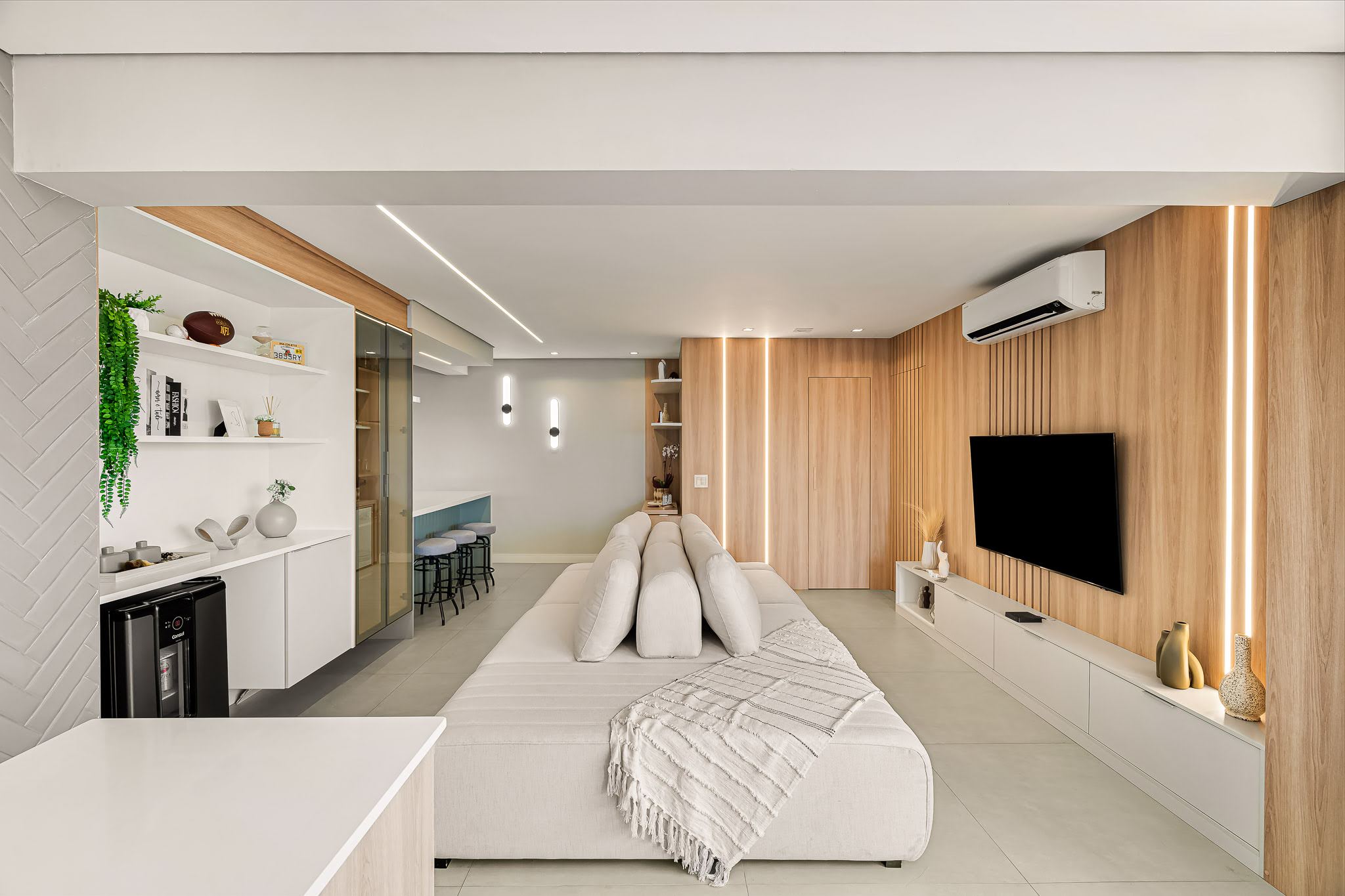 Vista ampla do living com painel de TV ripado em madeira, rack suspenso branco e ar-condicionado embutido