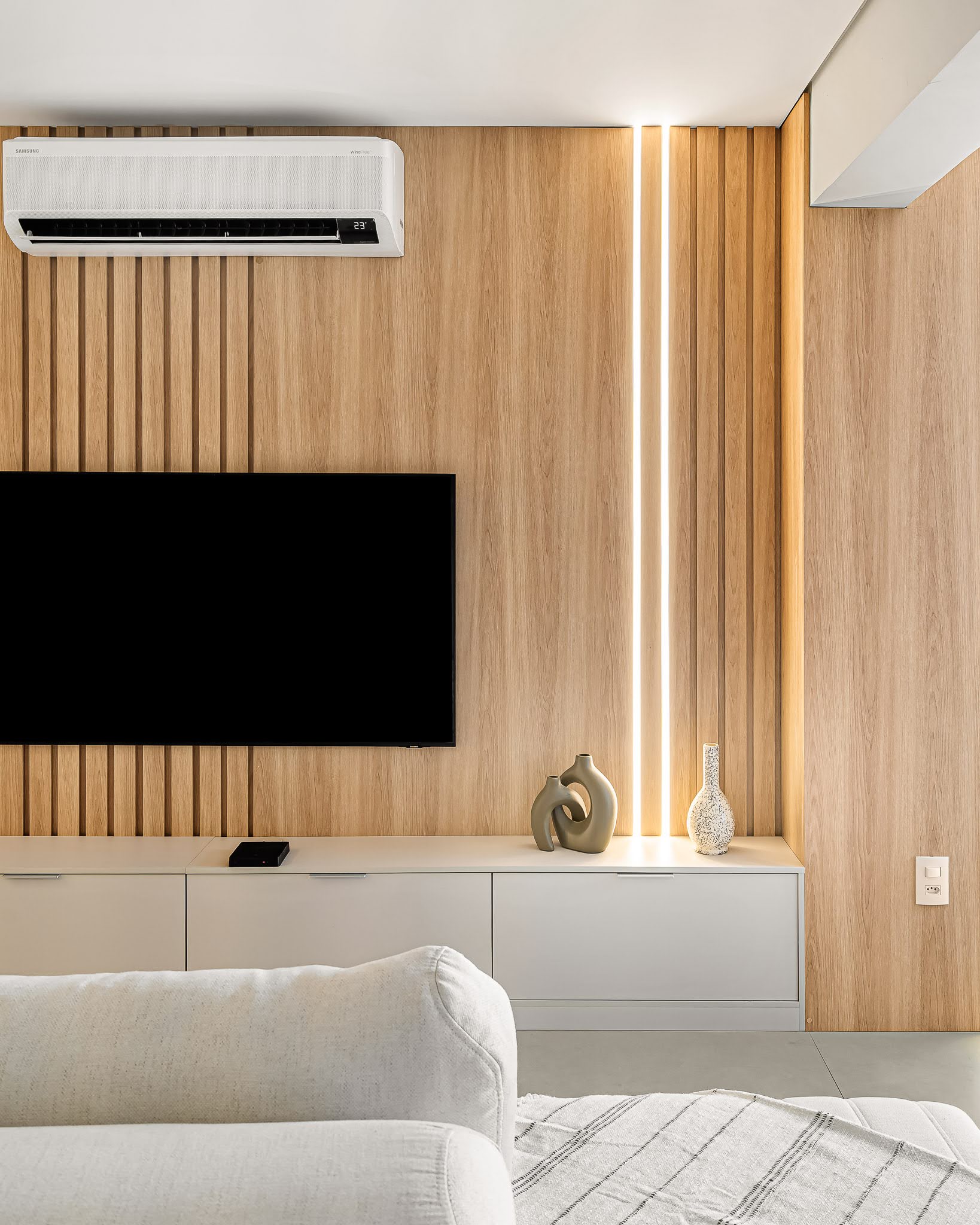 Detalhe do painel de TV em madeira com fita de LED vertical e vasos decorativos