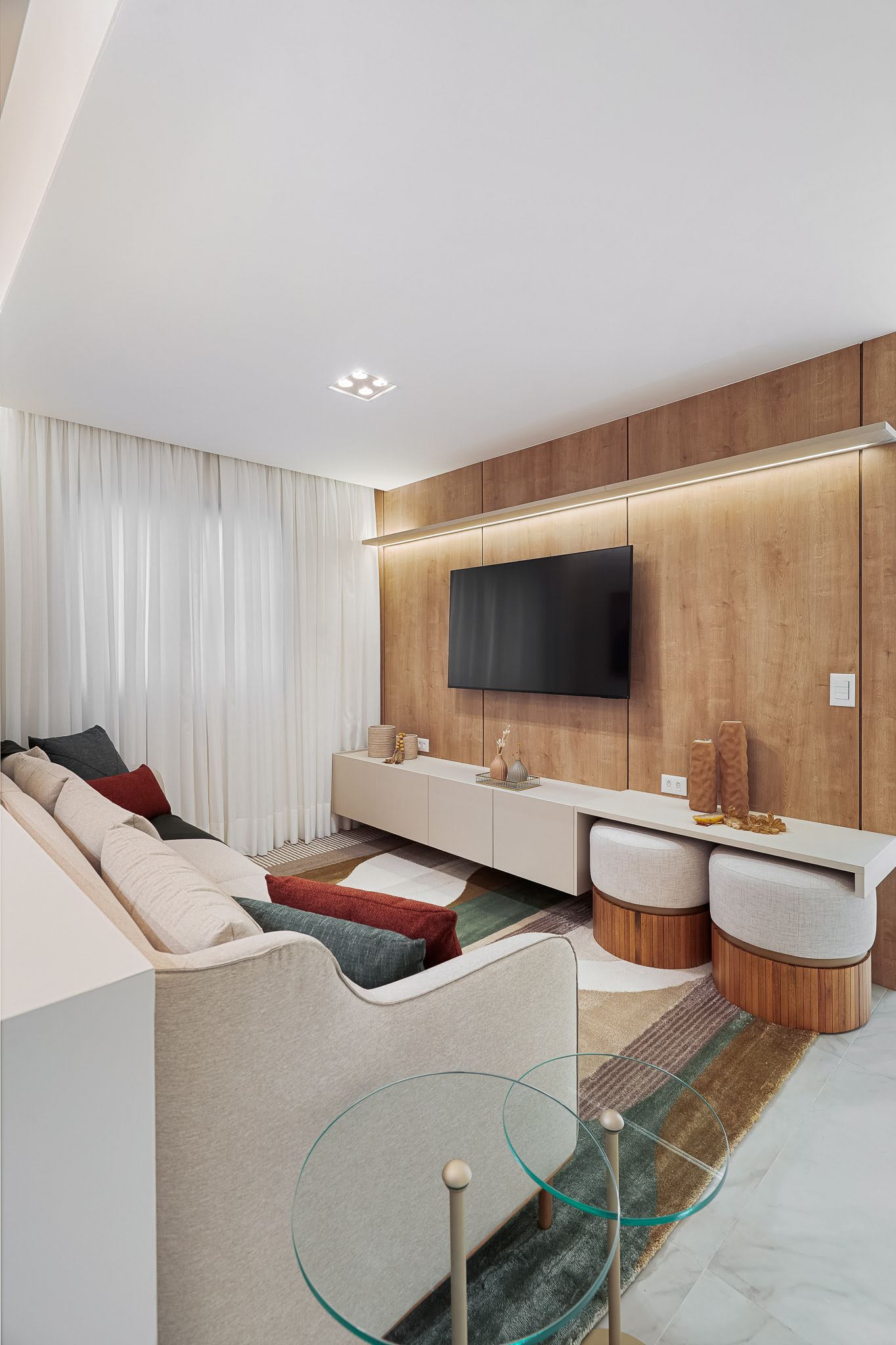 Living com painel de madeira, rack suspenso e pufes em tons claros
