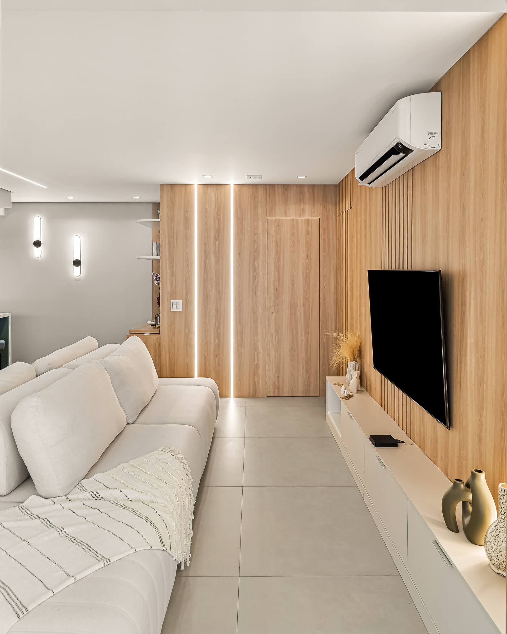 Living com sofá claro, arandelas pretas e painel de madeira com iluminação linear