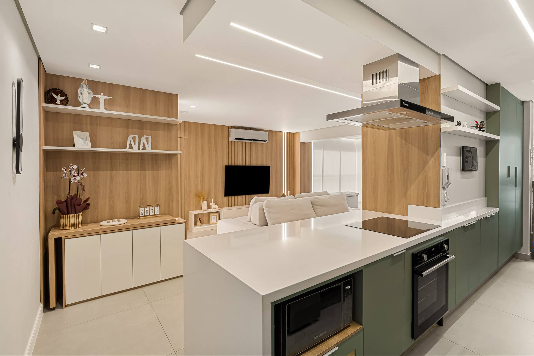 Cozinha com armários verdes, prateleiras brancas, coifa em inox e painel de madeira decorado
