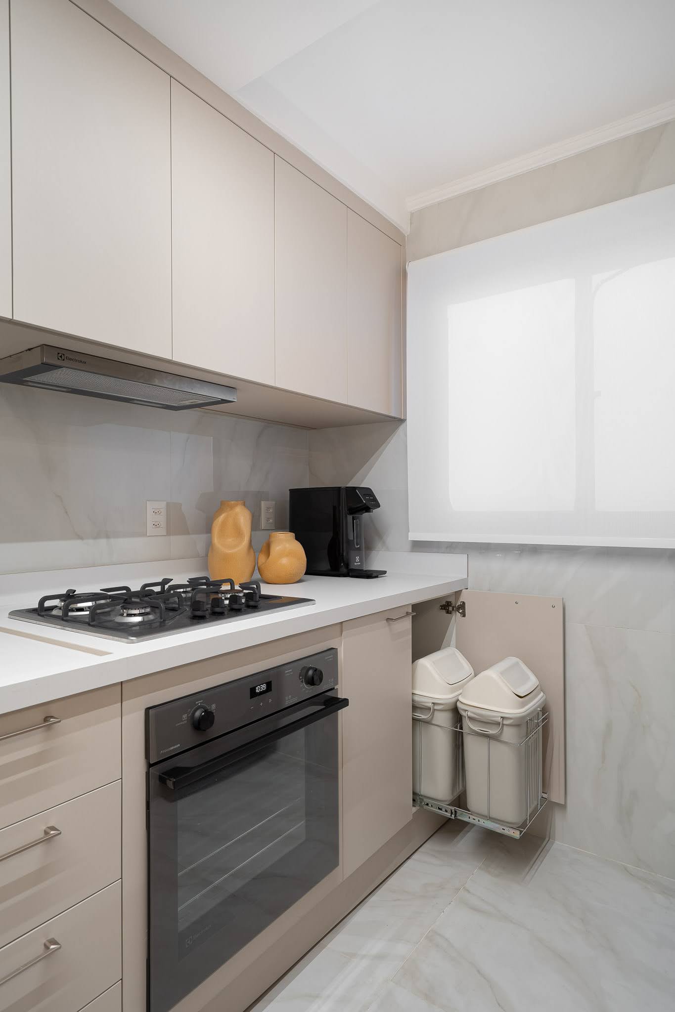 Detalhe da cozinha com gaveta de lixeiras embutidas e marcenaria neutra