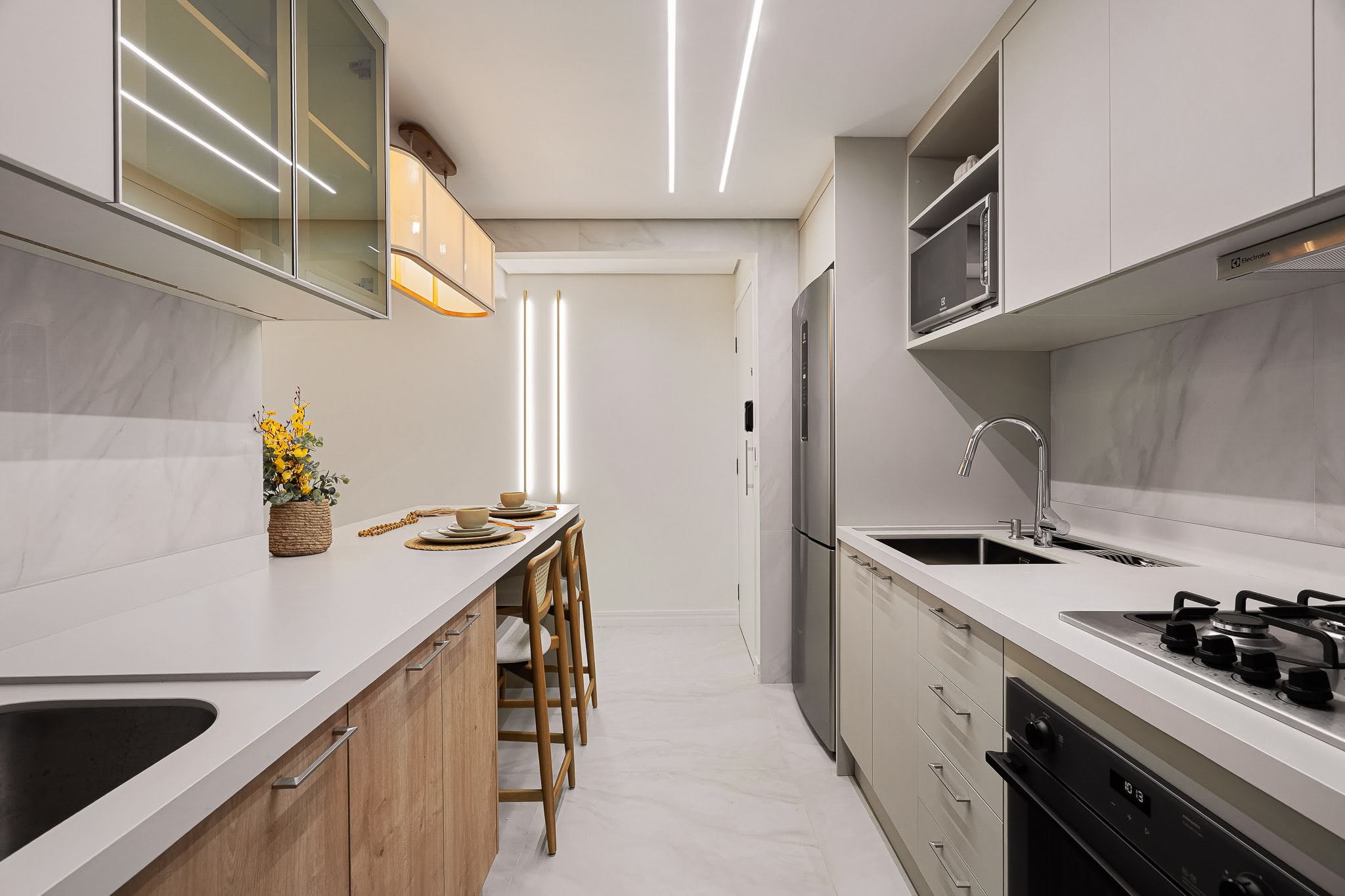 Bancada da cozinha com banquetas em madeira e iluminação linear no teto