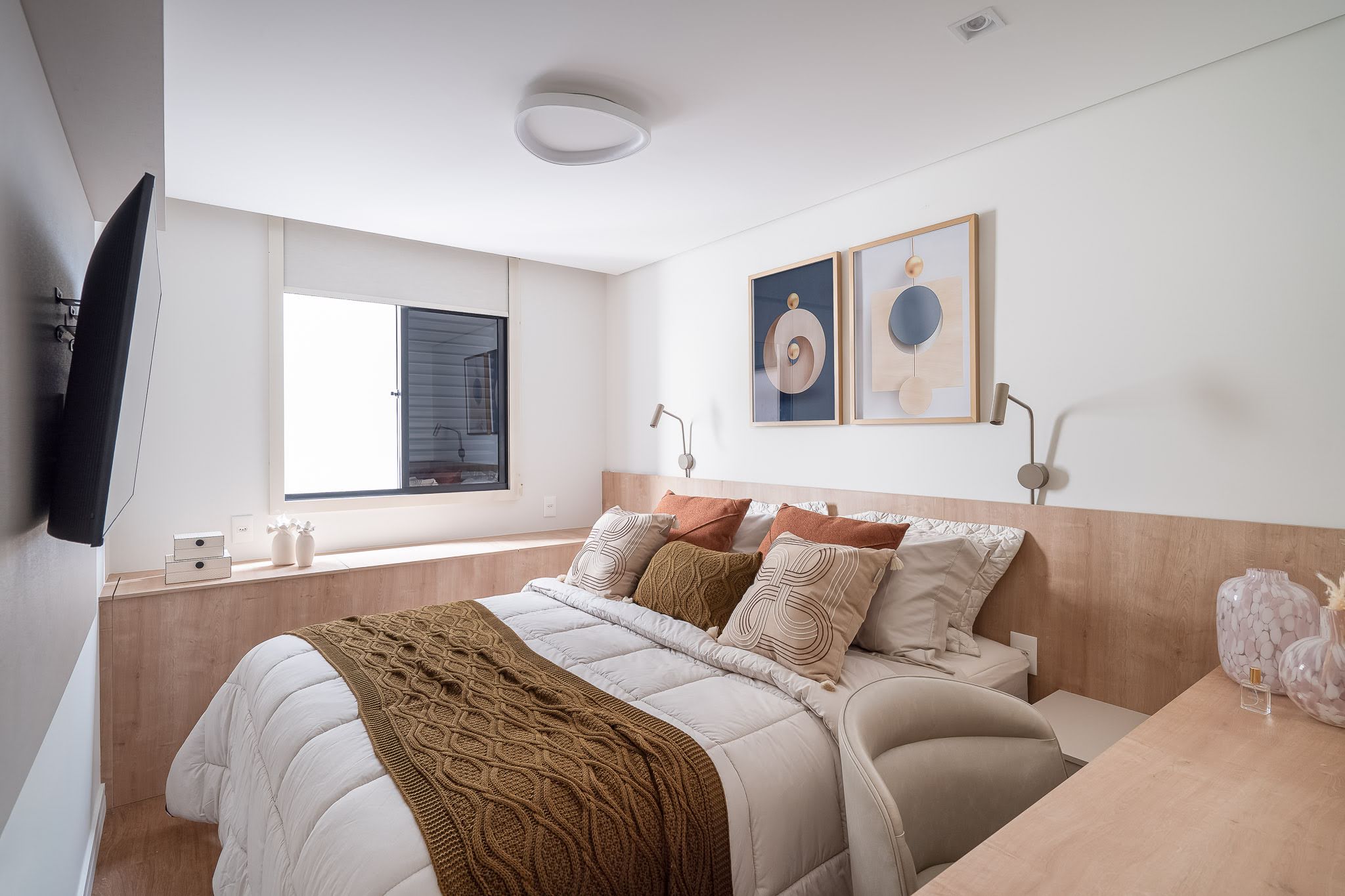 Quarto com cabeceira em madeira clara, quadros e manta em mostarda