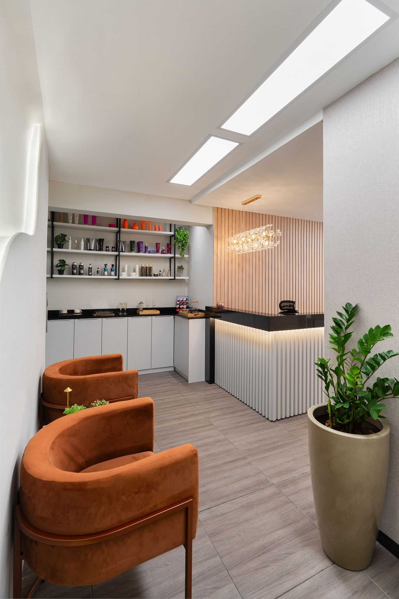 Recepção vista das poltronas em veludo terracota, com estante de produtos e planta